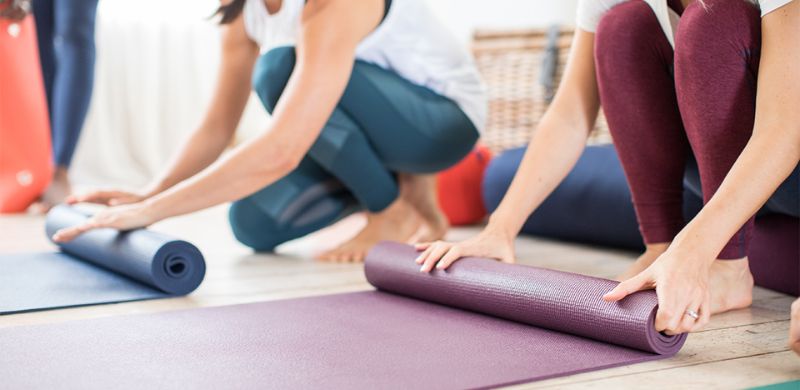 People rolling out their yoga mats, symbolizing a simple, stress-free start to practicing yoga in a comfortable space.