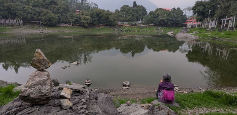 A person meditating and gazing at a calm lake in nature, symbolizing mindfulness, inner stillness, and the practice of observation in yoga.