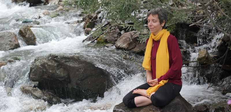 A person meditating beside a river, practicing mindful breathing to cultivate calm and presence.