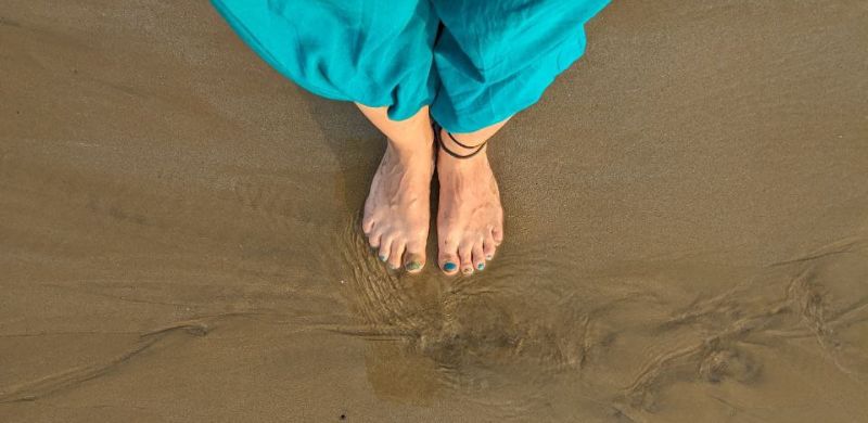 Bare feet standing on wet beach sand, a moment of calm and grounding.